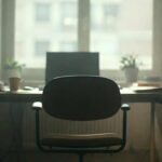 An empty office chair with a box of belongings symbolizing layoff stress and emotional impact.