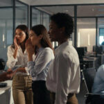 Office gossip showing coworkers whispering while one employee feels isolated in a corporate office